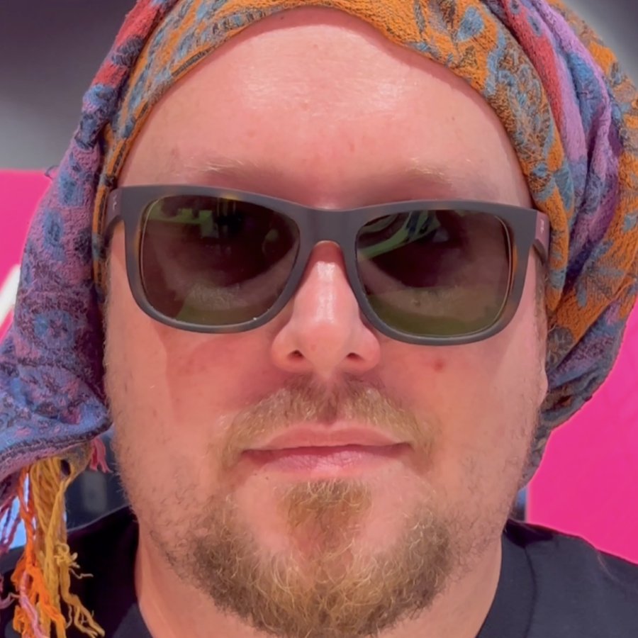 Verkleidete Person mit Sonnenbrille und buntem Kopftuch als humorvolles Video-Vorschaubild für den Telekom Shop St. Ingbert